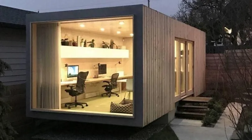 Instalación eléctrica en contenedores Oficina modular iluminada de noche, con focos empotrados encendidos y dos puestos de trabajo: electricidad para contenedores