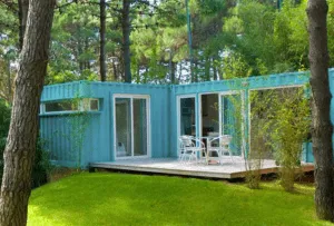 Vivienda de dos contenedores marítimos turquesa en L con tarima de madera y pinos