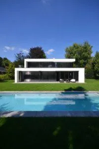 Casa moderna blanca de dos plantas con grandes ventanales, césped y piscina rectangular en primer plano