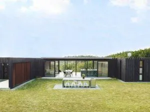 Vivienda de una planta con módulos tipo contenedores marítimos revestidos de madera negra y salón acristalado