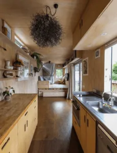 Cocina alargada de madera con fregadero de acero y sofá al fondo en una casa contenedor