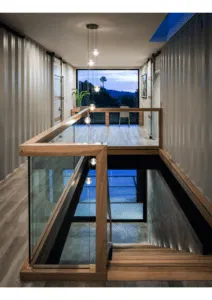 Interior de casa con contenedores marítimos de chapa ondulada, con escalera y barandilla de cristal