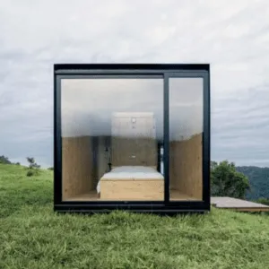 Cabaña negra con frente de cristal y dormitorio forrado de madera sobre una ladera verde
