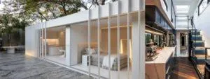 Casa con contenedores marítimos: módulo blanco con dormitorio abierto al patio y cocina con escalera