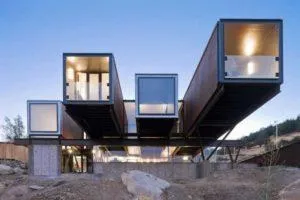 Casa con contenedores marítimos en voladizo sobre base de hormigón, iluminada al anochecer entre rocas