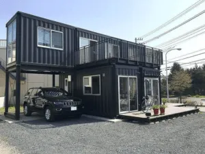 Casa de contenedores negra de dos plantas con cochera abierta, terraza arriba y tarima con bicicleta