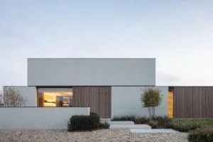 Casa minimalista gris de líneas rectas con listones de madera y ventanal iluminado al anochecer
